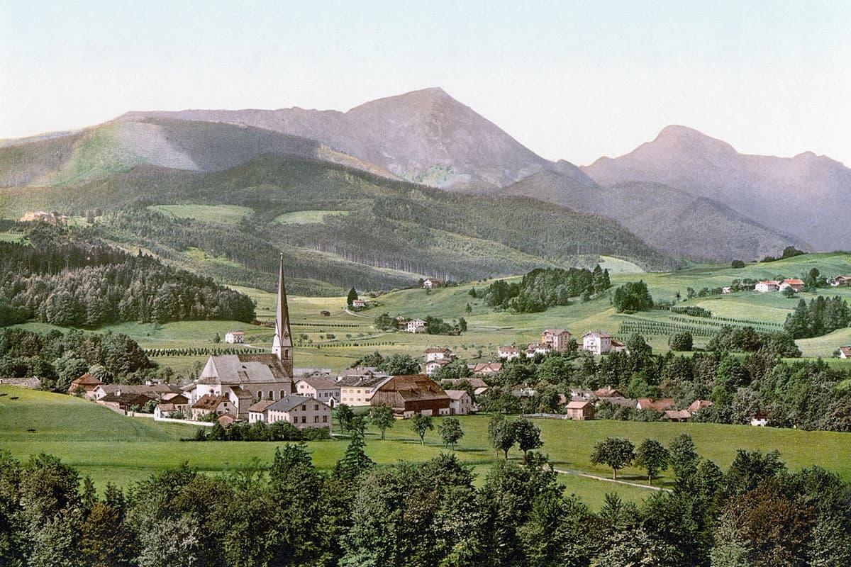 Historische Ansicht von Siegsdorf mit Pfarrkirche, Wiesen und Bergen im Hintergrund.